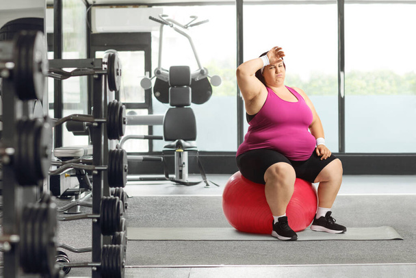 Tired overweight woman sitting on a fintess ball at the gym - Fotografie, Obrázek