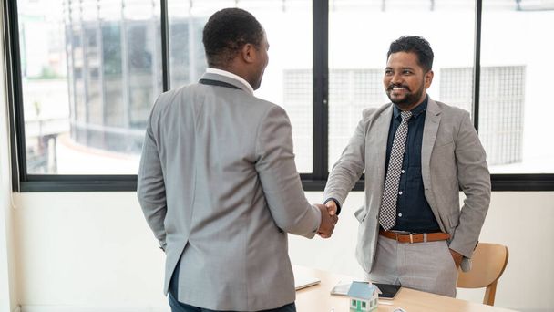 A professional and smiling Indian-Asian businessman shakes hands with an African American business partner after a meeting. Greeting, welcome, congratulations, diverse business people - Photo, Image