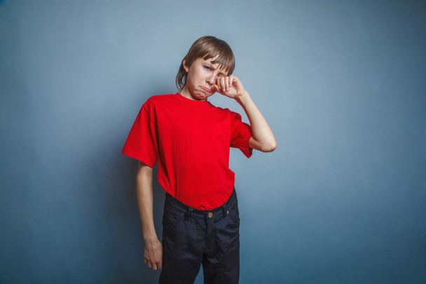 Niño, adolescente, doce años en la camiseta roja, las manos se secan las lágrimas
 - Foto, Imagen