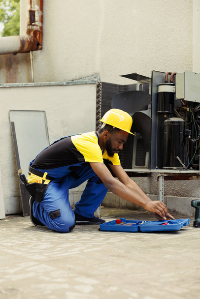 Adept afrikanisch-amerikanische Reparaturfirma beginnt Routinewartung auf externe HVAC-System, Vorbereitung Werkzeugkiste. Techniker bereitet Werkzeuge für die Überprüfung defekter Teile der Klimaanlage vor - Foto, Bild