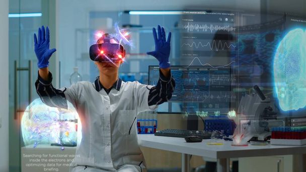 Professionnel scientifique en clinique de recherche portant un casque VR, utilisant un équipement de pointe et des capteurs câblés pour faire des expériences. Médecin utilisant la technologie de réalité virtuelle pour visualiser les données de neurologie médicale - Photo, image