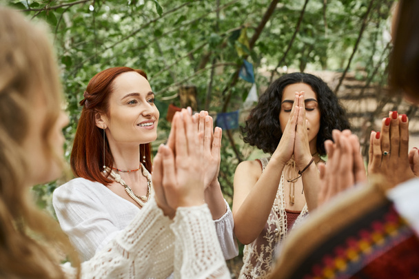 sonriente pelirroja meditando con amigos multiétnicos al aire libre en el centro de retiros - Foto, Imagen