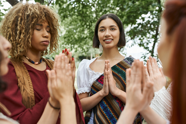 pozitivní mladá žena v boho oblečení meditace v blízkosti multietnické přátele venku v centru ústupu - Fotografie, Obrázek