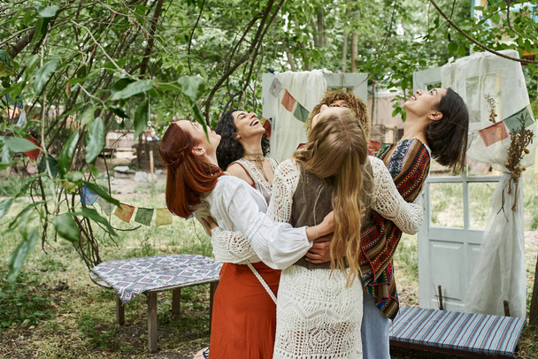 joyful and interracial women friends in boho outfits hugging outdoors in retreat center - Foto, immagini