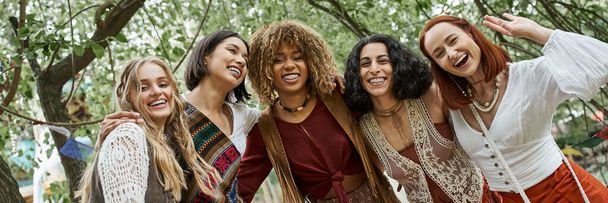 cheerful interracial women in boho styled clothes looking at camera in retreat center, banner - Photo, Image