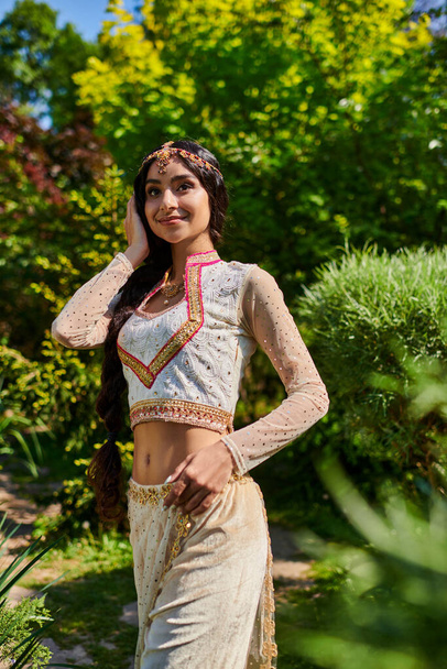 young and pleased woman in elegant traditional clothes looking away in summer park - Foto, imagen