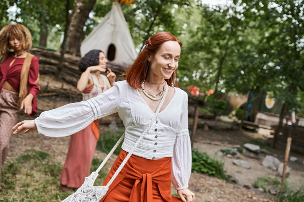 cheerful redhead woman in boho outfit spending time near multiethnic women in retreat center - Photo, Image