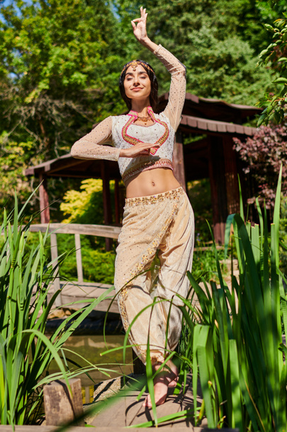 verano relajarse, elegante mujer india en ropa tradicional bailando con los ojos cerrados en el parque verde - Foto, Imagen