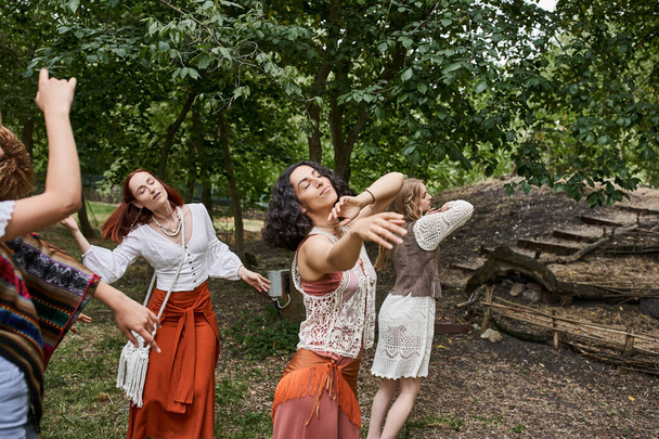 multiethnic girlfriends in stylish clothes dancing with closed eyes in outdoor retreat center - Photo, Image