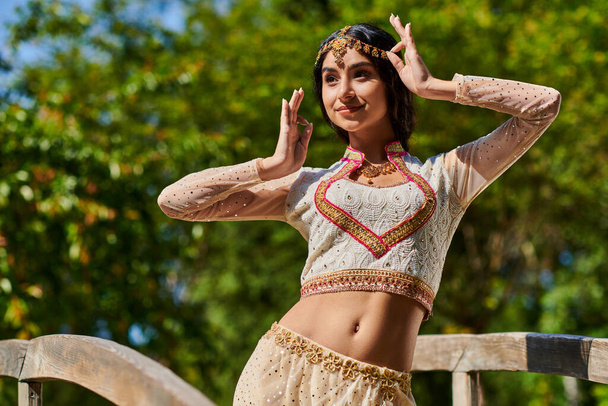 cheerful indian woman in vibrant traditional attire posing in park on sunny summer day - Fotografie, Obrázek