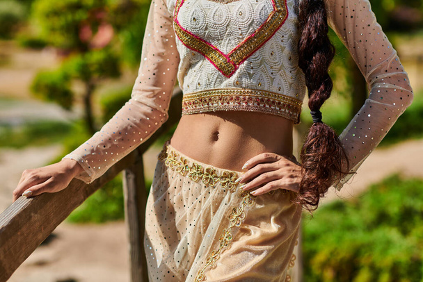 καλλιεργημένη άποψη της ινδικής γυναίκας με παραδοσιακά ρούχα στέκεται με το χέρι στο ισχίο στο πάρκο το καλοκαίρι - Φωτογραφία, εικόνα