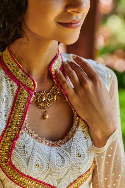 περικοπή άποψη του χαμογελαστού ινδική γυναίκα σε παραδοσιακή ενδυμασία και κολιέ κοσμήματα που θέτουν σε εξωτερικούς χώρους - Φωτογραφία, εικόνα