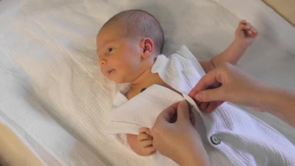 Mother dressing her newborn baby indoors. A cute newborn lies on a changing table, parental care and love. New life. - Footage, Video