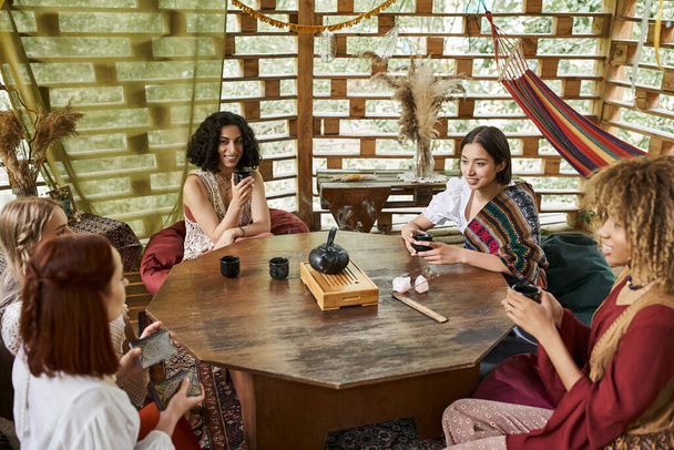 women retreat concept, positive multiethnic girlfriends drinking tea and talking at wooden table - Foto, Imagem