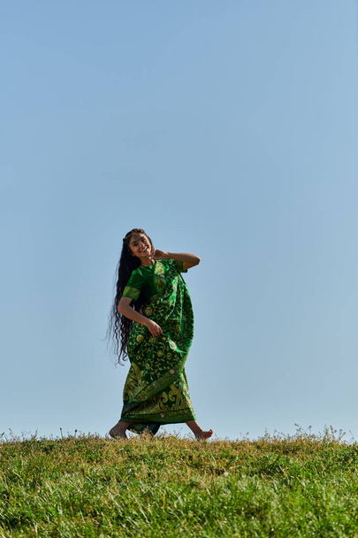 Yaz tatili, kaygısız Hintli kadın sari ile yeşil çayırlarda yürüyor mavi bulutsuz gökyüzünün altında - Fotoğraf, Görsel