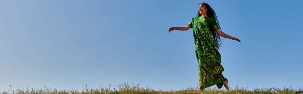 carefree summer, elegant indian woman in traditional sari running under blue cloudless sky, banner - Photo, Image