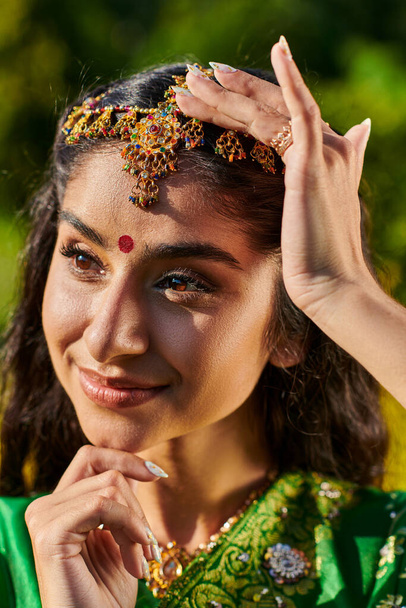 portrait of stylish and cheerful indian woman with bindi and matha patti standing outdoors - Foto, Imagen