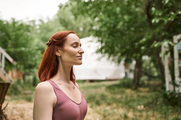 happy redhead woman meditating with closed eyes in retreat center outdoor - Photo, Image