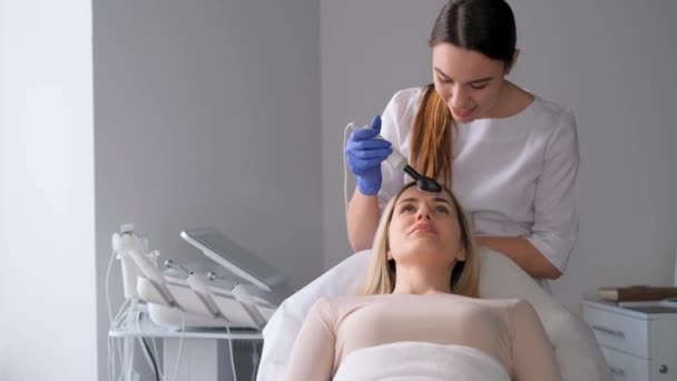 Kosmetolog provádí pro ženu proceduru čištění pleti obličeje. Postup na ultrazvukovém přístroji pro obličej. - Záběry, video