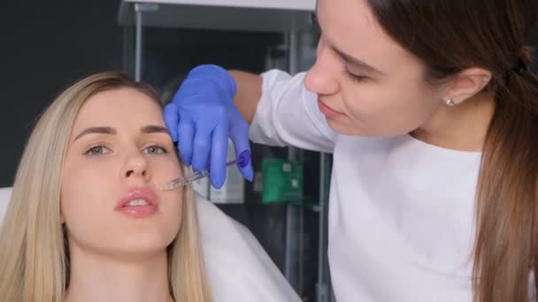 Giovane donna bionda ottiene un'iniezione nelle labbra in un salone di bellezza. Una bionda riceve un'iniezione nelle labbra, il concetto di una procedura estetica e cosmetica. - Filmati, video