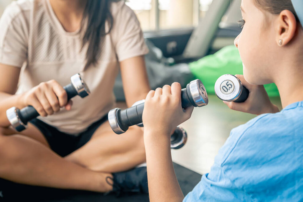 A woman with the daughter doing sports with dumbbells at gym on the floor, mother and baby are happy to train together. - Photo, Image