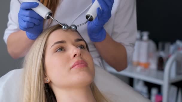 Un'estetista usa impulsi elettrici per una procedura facciale. Donna sottoposta a lifting facciale con procedura microcorrente. Video verticale - Filmati, video