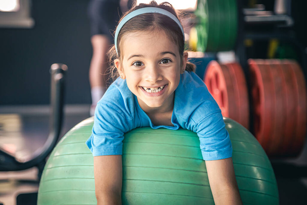 Chica feliz estira su cuerpo en un fitball en el gimnasio, gimnasia y pilates para niños. - Foto, imagen