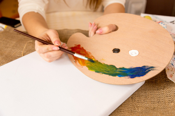 Close-up shot van vrouwelijke kunstenaar mengen olieverf op houten pallet - Foto, afbeelding