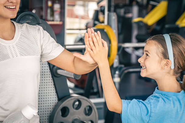 Beautiful strong woman and charming little daughter giving high five at gym. - Photo, Image