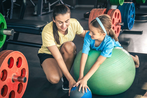 Little sporty girl and young beautiful mother doing stretching with fitness ball at gym. - Photo, Image