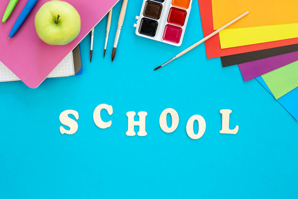 Kolorowe materiały szkolne i drewniane litery na niebieskim tle, powrót do koncepcji szkoły, widok z góry. - Zdjęcie, obraz