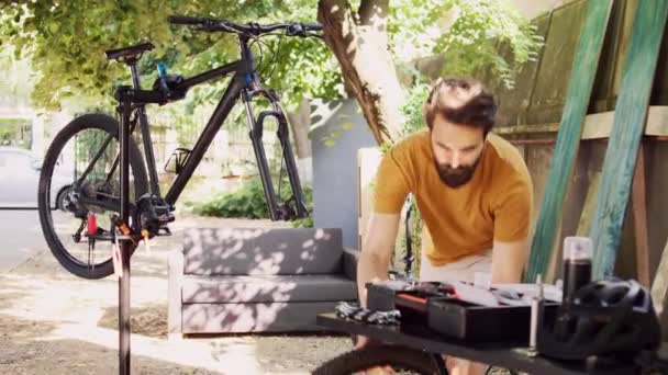 Youthful caucasian man outside with professional equipment adjusting and maintaining bicycle parts. Determined male detaching broken wheel and examining bike components. Dolly zoom-in. - Footage, Video