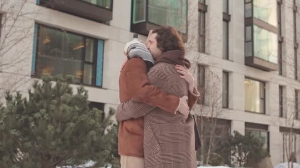 Two young Caucasian men in love embracing each other with tenderness, standing outdoors in urban environment on cold winter day - Footage, Video
