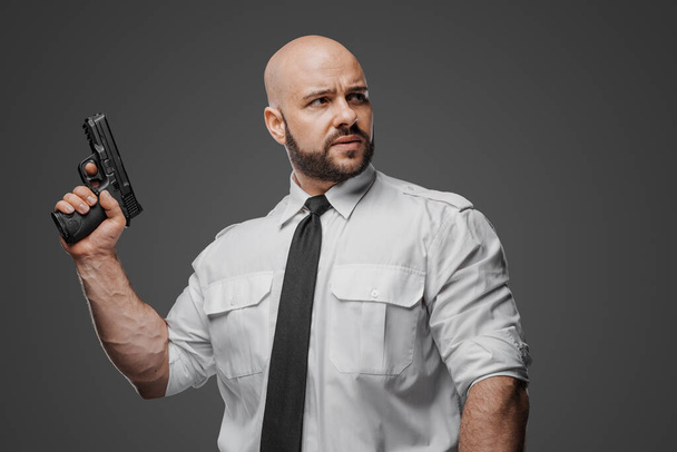 Forte individuo barbuto in abito bianco frizzante prepara la sua arma da fuoco, suggerendo ruoli di sicurezza o detective - Foto, immagini