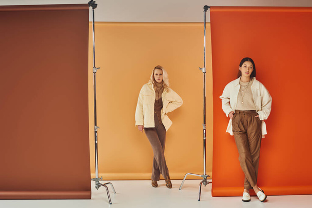 fall fashion, young interracial women in stylish attire posing on pastel multicolored backdrop - Photo, Image