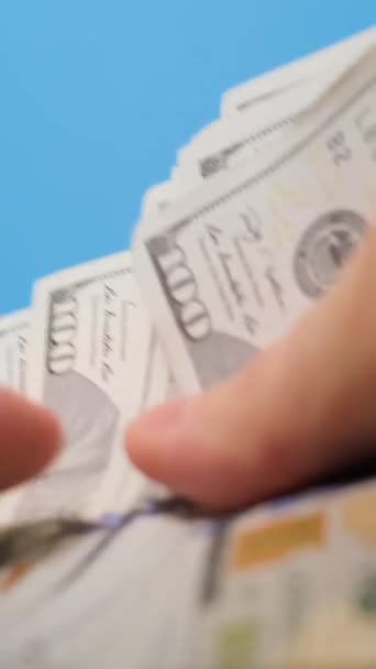 Primer plano de un hombre europeo contando dinero en dólares sobre un fondo azul. Presupuesto familiar, efectivo. Vídeo vertical - Metraje, vídeo