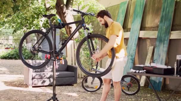 Sağlıklı erkek bisikletçi dikkatle bisikletin hasarlı lastiğini gevşetiyor ve söküyor. Sportif genç adam dikkatli bir şekilde bisiklet tekerleğini çözüyor ve ön çatalı ev bahçesine yerleştiriyor.. - Video, Çekim