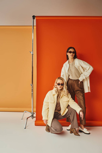 moda e estilo, modelos inter-raciais em óculos de sol e outerwear posando em estúdio, cores de outono - Foto, Imagem