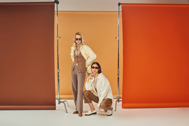 interracial models in sunglasses and autumn attire posing on colorful backdrop, fall colors - Photo, Image