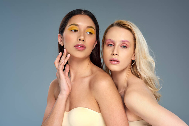 diverse young models with bold eye makeup posing together on blue backdrop, beauty trend concept - Foto, Imagem