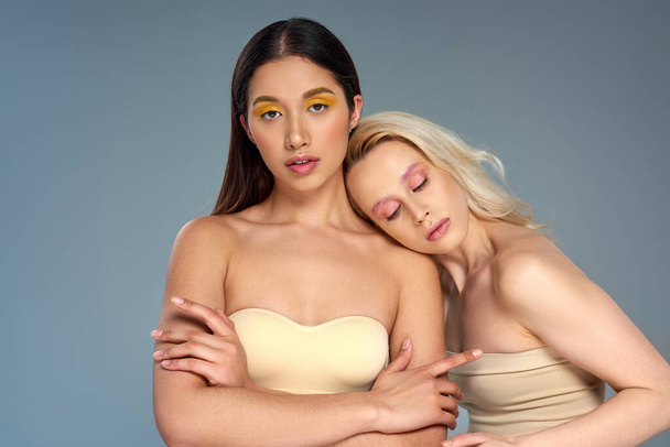 interracial models with trendy eye makeup looking at camera on blue backdrop, diverse beauty concept - Photo, Image