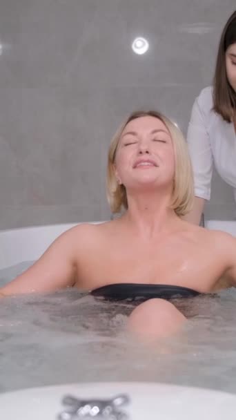 Una mujer relajada recibe un hidromasaje de un esteticista profesional en un centro de spa. Tratamiento de la espalda con la ayuda de procedimientos de agua. Vídeo vertical - Imágenes, Vídeo