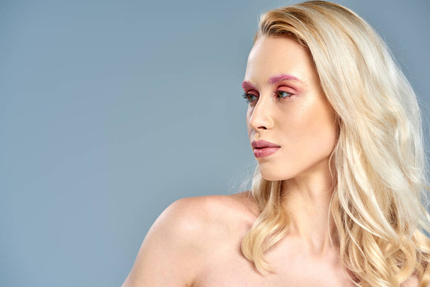αισθησιακό μοντέλο με ροζ μακιγιάζ ματιών και ξανθά μαλλιά που κοιτούν μακριά σε γκρι φόντο, θηλυκή ομορφιά - Φωτογραφία, εικόνα