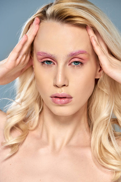 captivating model with pink eye makeup and blonde hair posing on grey backdrop, feminine beauty - Photo, Image