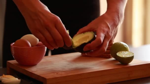 vrouw handen voorbereiding avocado voor eten close-up op houten plank thuis - Video