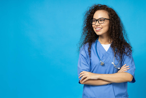 An attractive young girl in glasses and a blue nurse's uniform on a blue background - Fotó, kép
