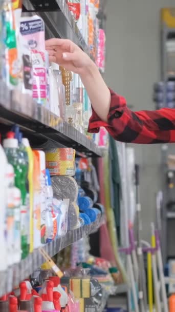 Ένα όμορφο κορίτσι με ένα καλάθι στα χέρια της κάνει αγορές σε ένα κατάστημα οικιακών χημικών ουσιών. Κάθετη βίντεο - Πλάνα, βίντεο