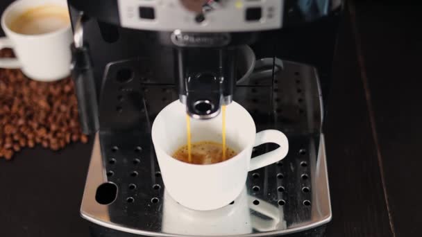 Uma máquina de café moderna derrama delicioso café em uma xícara branca de pé em um suporte de metal, close-up. Café. - Filmagem, Vídeo