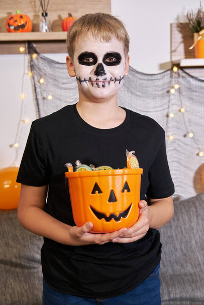 Het kind haalt het snoep uit de emmer voor Halloween. De jongen viert Trick or Treat. - Foto, afbeelding
