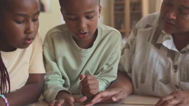 Afro-americano entre chico y chica y su abuela moderna resolviendo rompecabezas juntos en casa - Imágenes, Vídeo